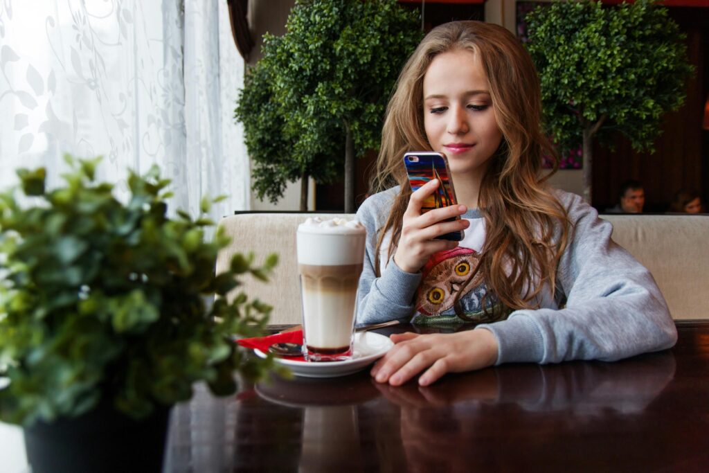 A young woman enjoys a latte while browsing her smartphone in a cozy cafe.