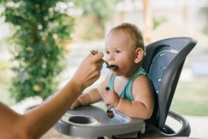Cute baby eating with a spoon in a high chair outdoors. Calm and precious moment.